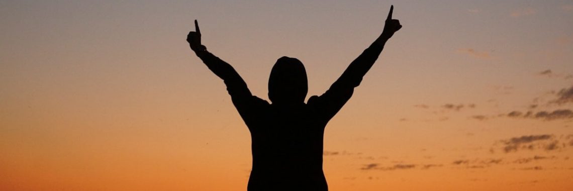 a person with their arms in the air at sunset